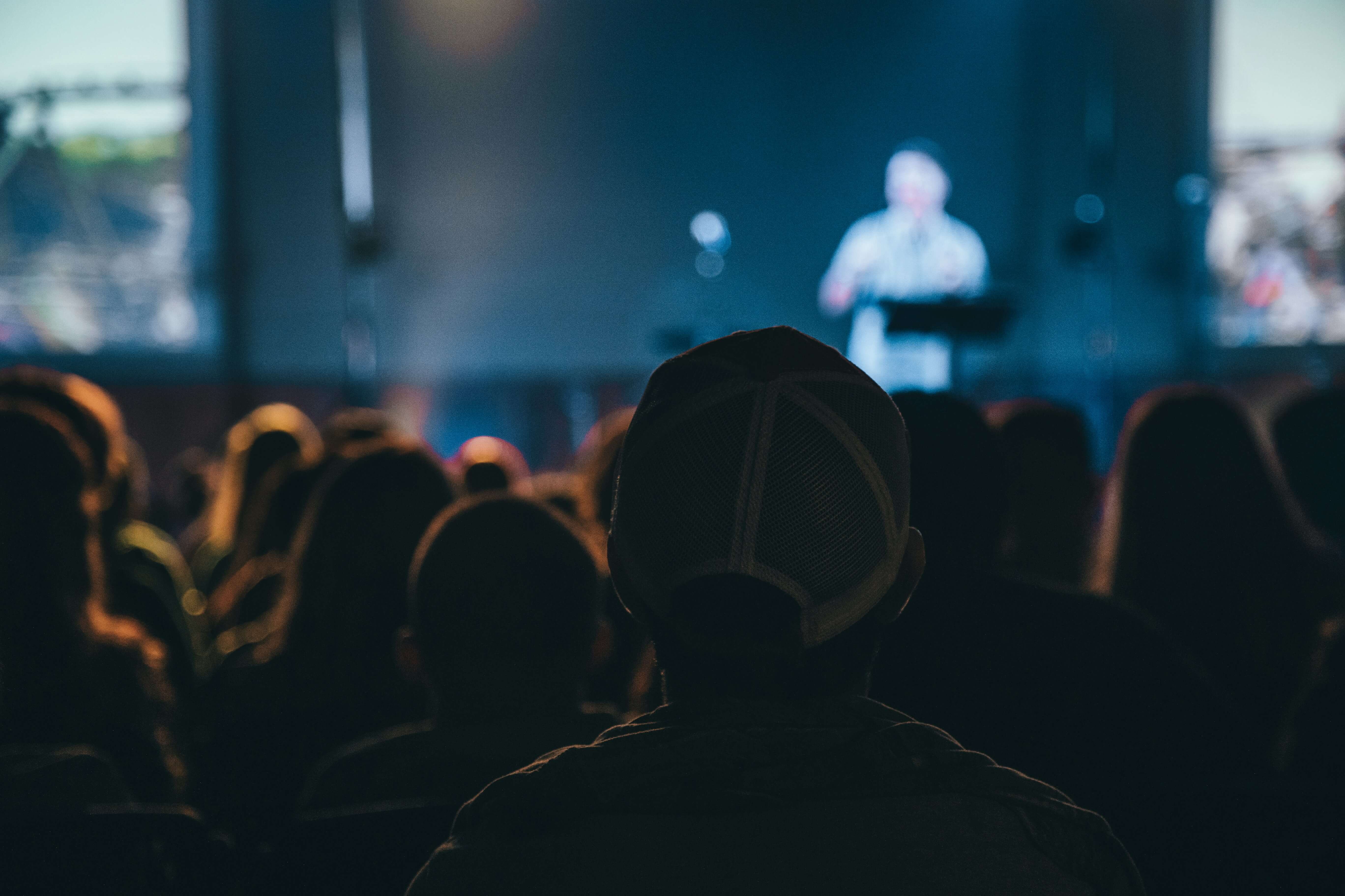 A person wearing a cap stands confidently in front of a large crowd